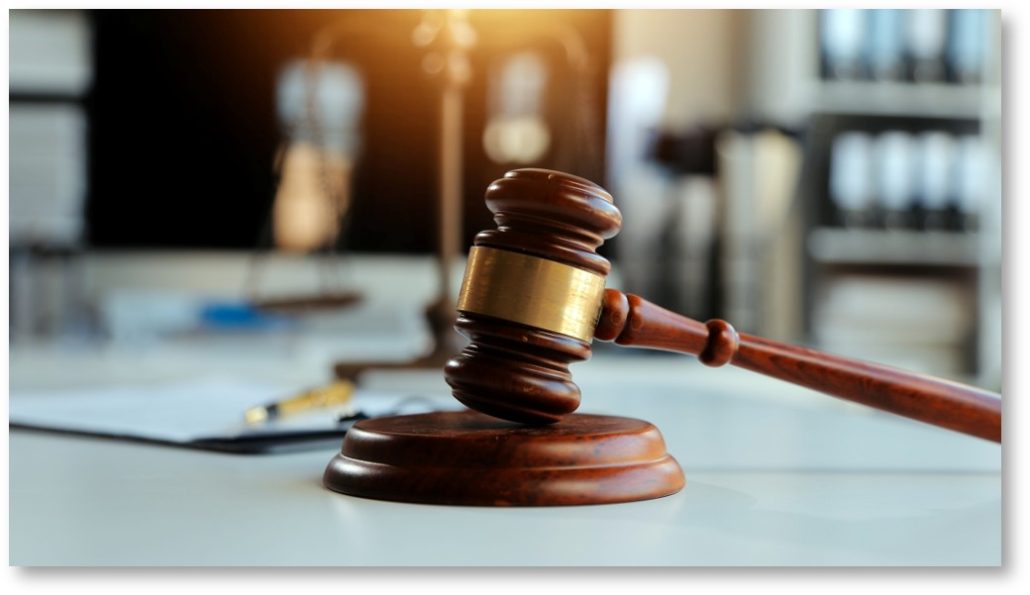 Holzrichterhammer liegt auf weißem Tisch vor unscharfem Hintergrund mit Aktenordnern