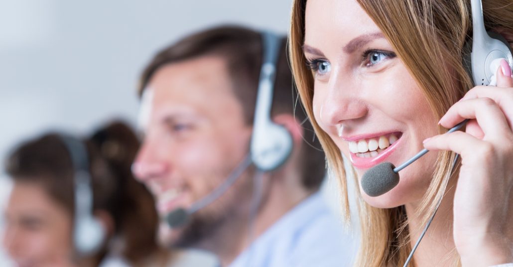 Im Vordergrund eine Telefonistin mit Headset und freundlichem Gesicht